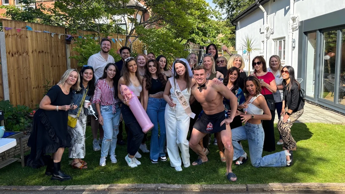 A butler that’s in the buff posing with guests at a garden hen party